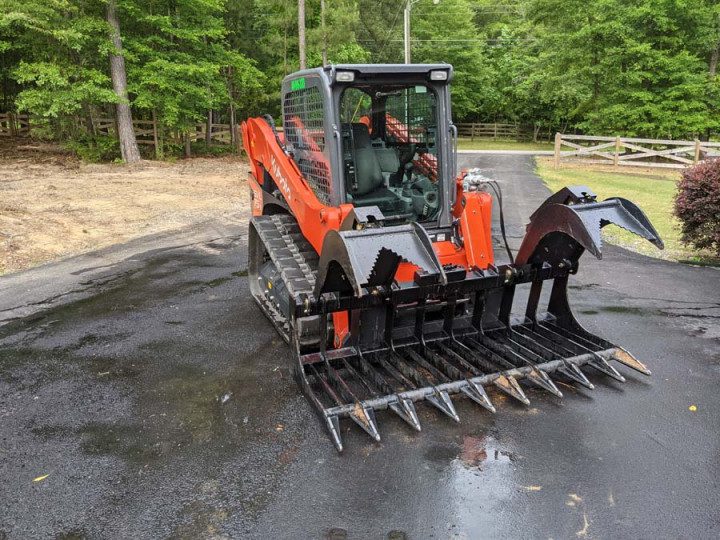 A man in an orange and black tractor with a grapple attachment.